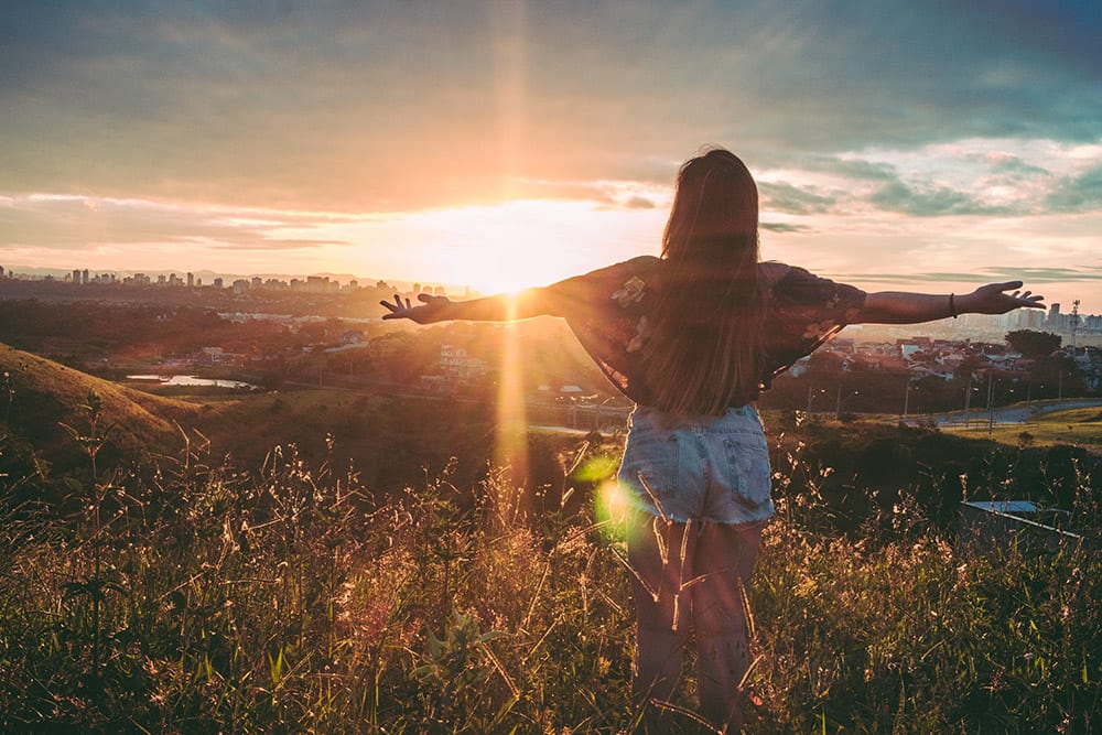 woman with outstretched arms looking towards sunset