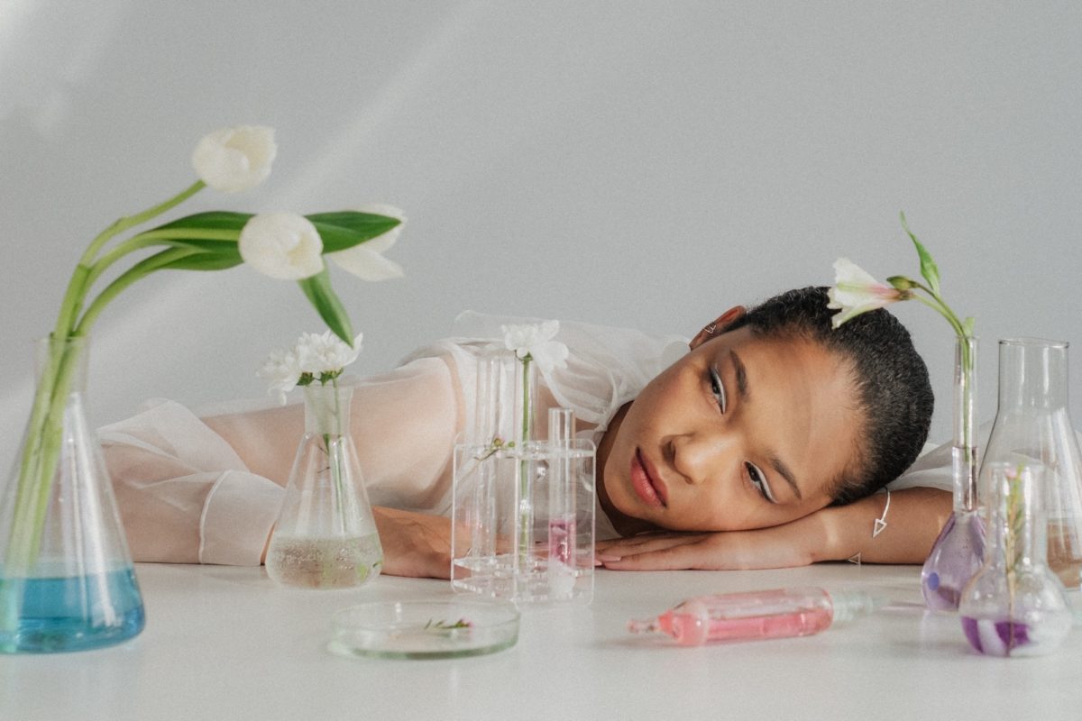 woman resting her head on table looking at beakers filled with flowers